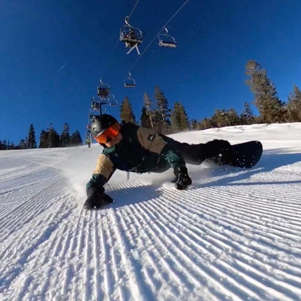 A snowboarder drags his hands with a flattened body while riding below a ski lift.
