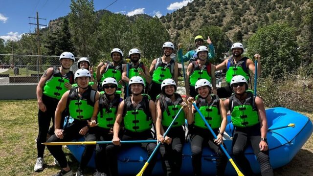 A group of rafters on a shored raft posing for a photo.