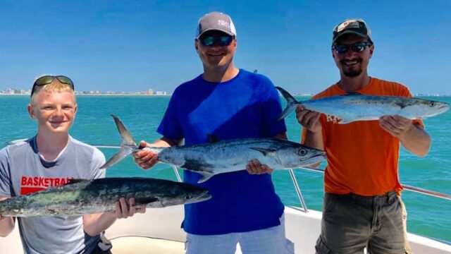 Two men and a teen hold three large fish on a boat.