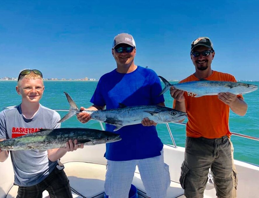 Two men and a teen hold three large fish on a boat.