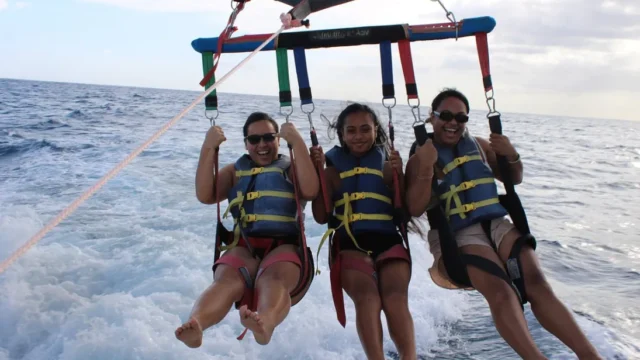 Three parasailers getting their feet dipped in the ocean.
