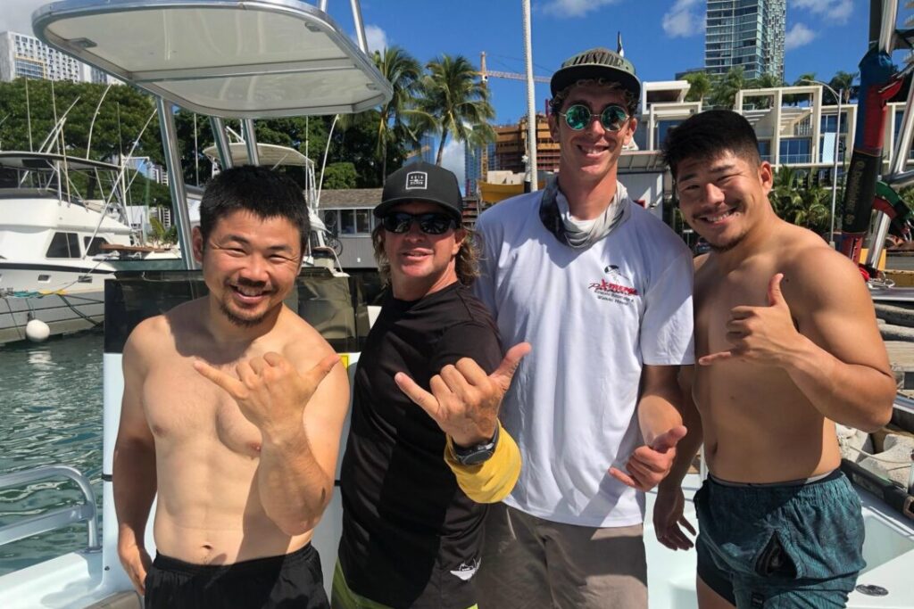 Four men throw shakas while smiling on a parasail boat.