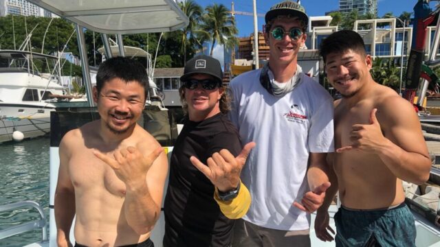 Four men throw shakas while smiling on a parasail boat.