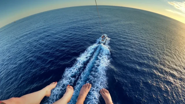 A parasailers view of the boat with two pairs of feet hanging.