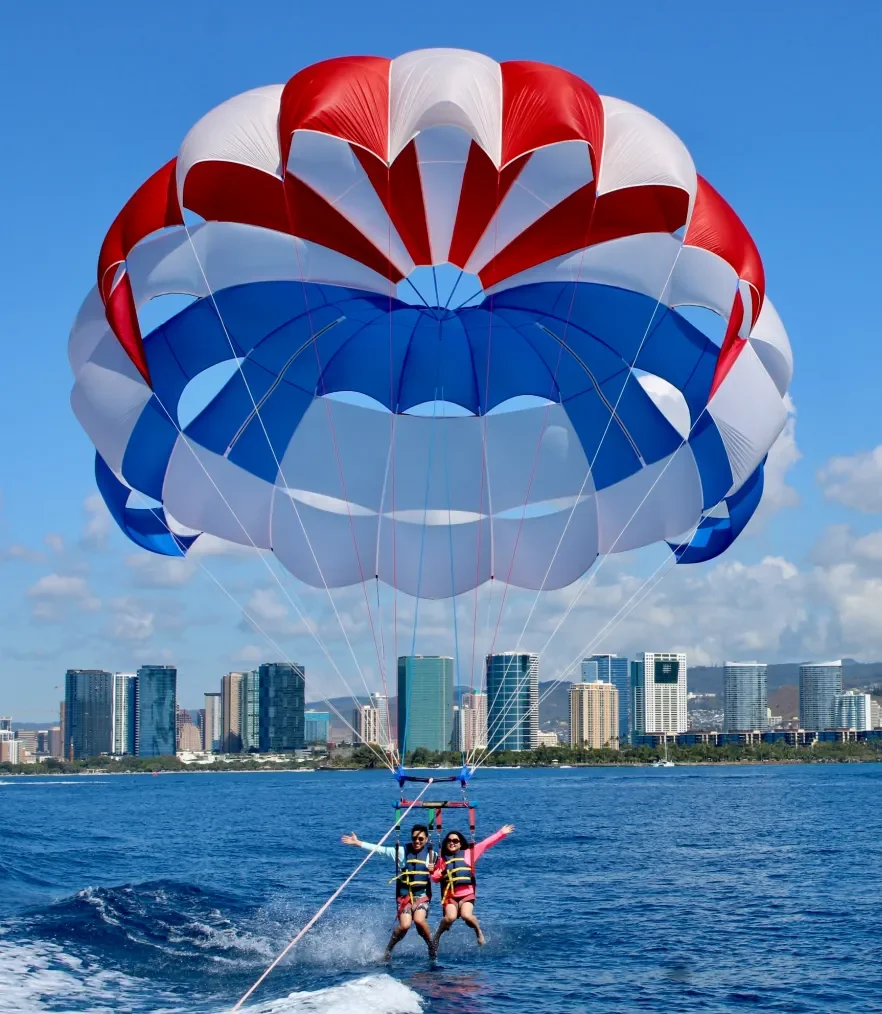 Parasailers getting dipped in the ocean with Honolulu's city in the background.