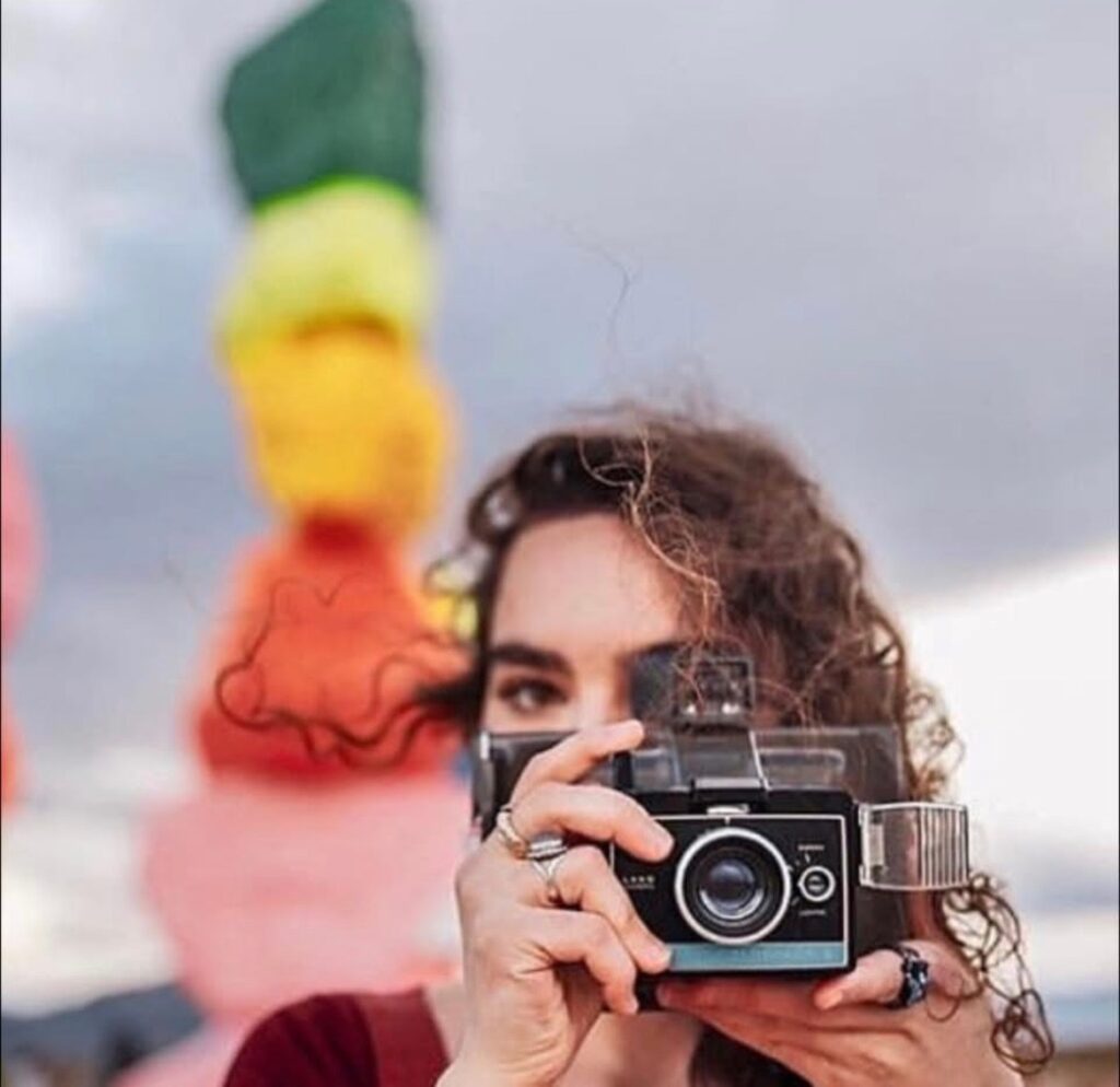 Photo of a girl taking a picture with a rainbow tower in the background.