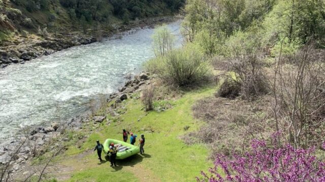 Two groups of people walking green rafts to the river with mountains in the background.
