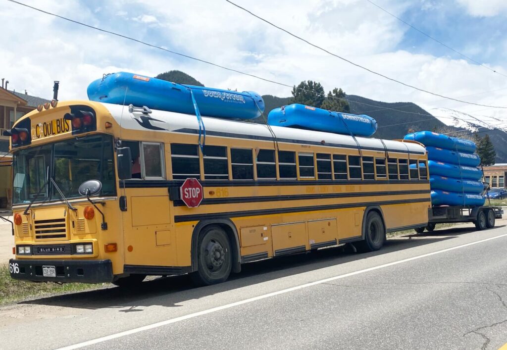 A school bus carrying blue rafts on top and trailer.