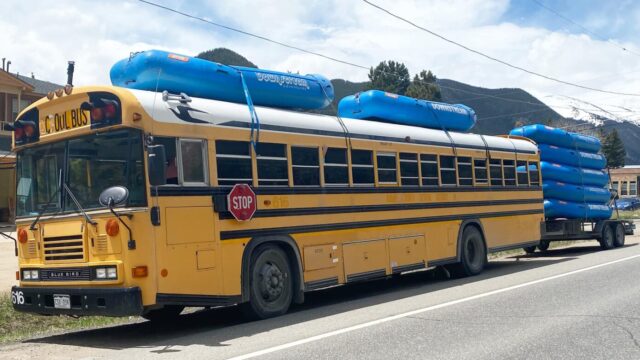 A school bus carrying blue rafts on top and trailer.