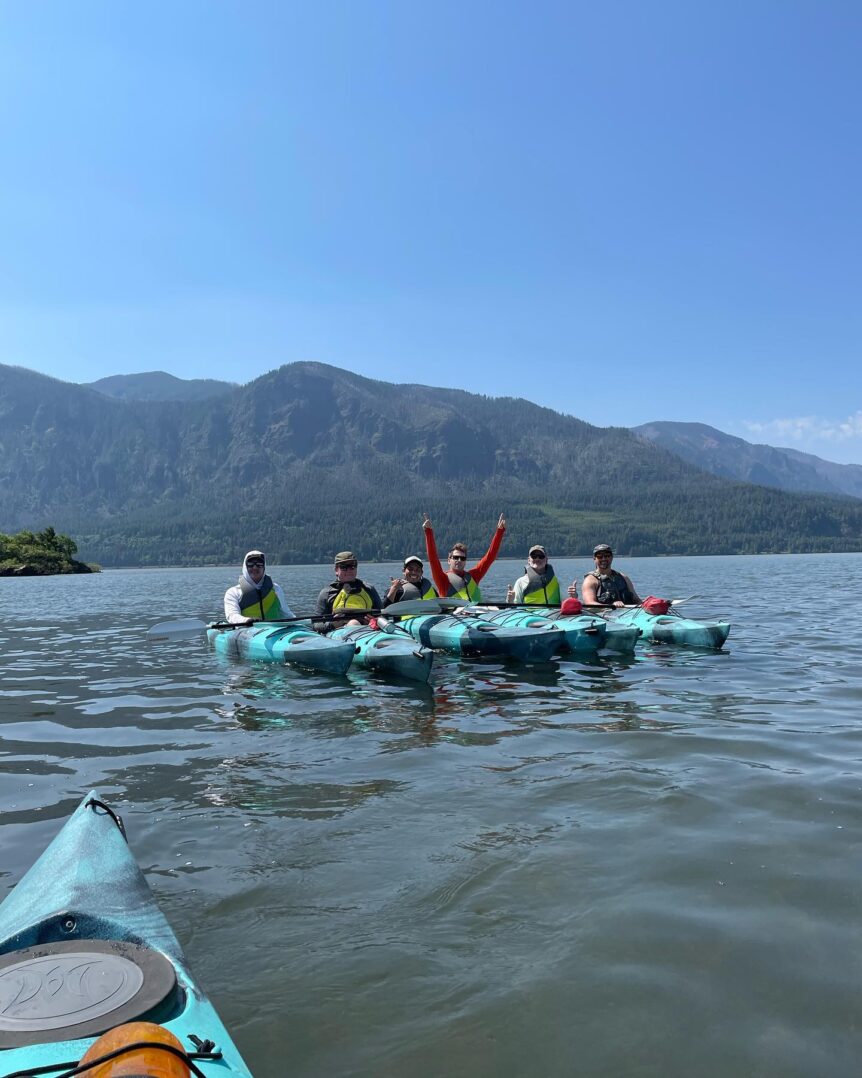 A group of kayakers pose in front of a mountain range.