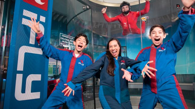 Family in iFly gear happy and ready to go flying with an instructor in the background flying in the tunnel