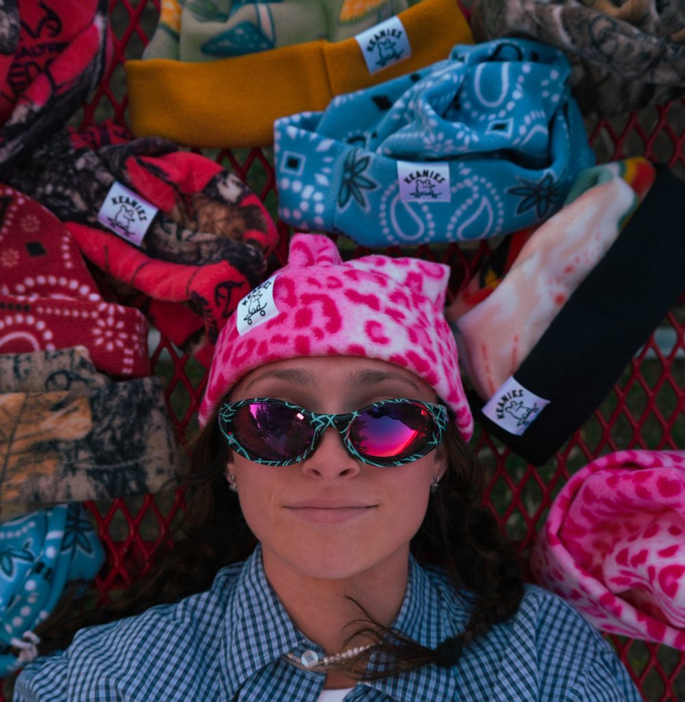 A girl in a Keanie Beanie with sunglasses surrounded by other hats.