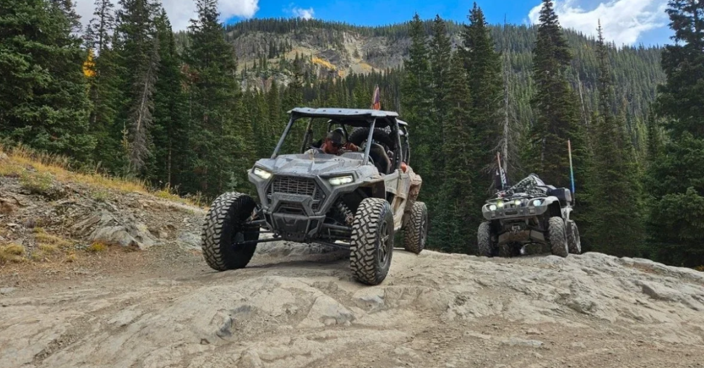 Two gray UTVs riding on a mountain trail.