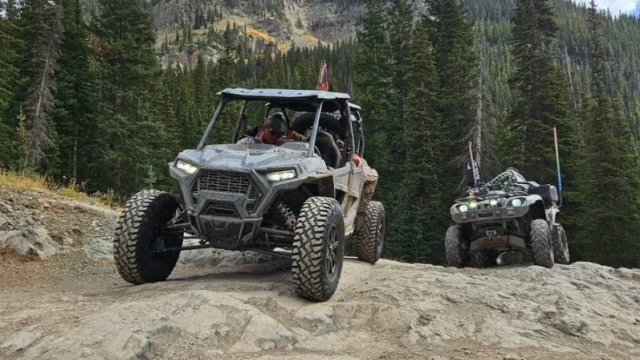Two gray UTVs riding on a mountain trail.