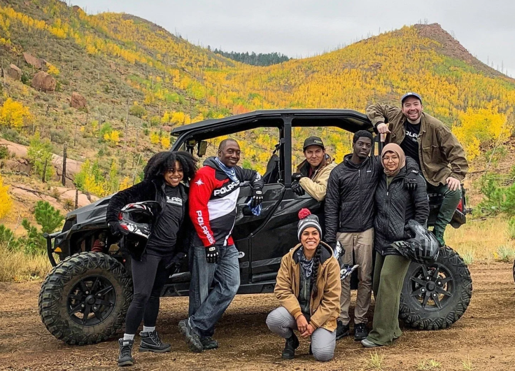 A group of people on a UTV vehicle in front of mountains.