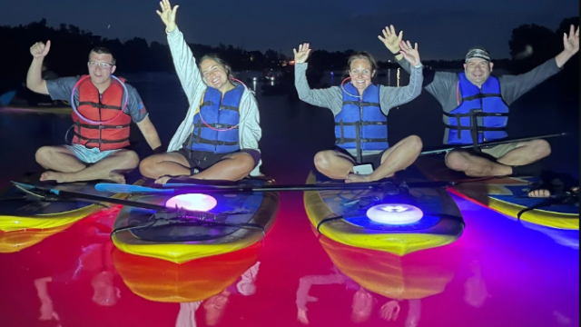 A group of paddleboarders on a lake at night.