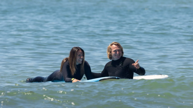 A man teaching a woman to surf.