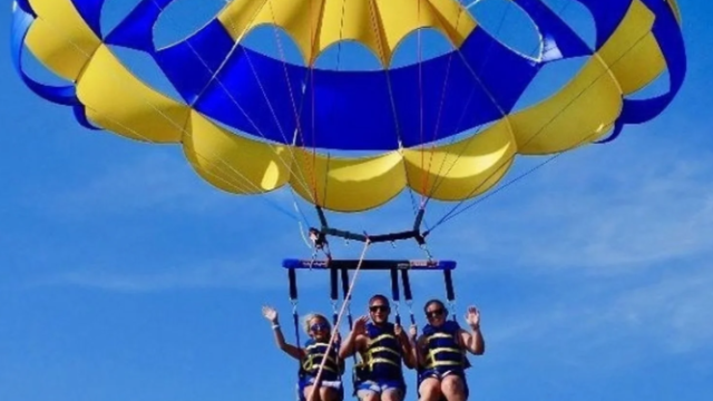 Three people parasailing over palm beach.