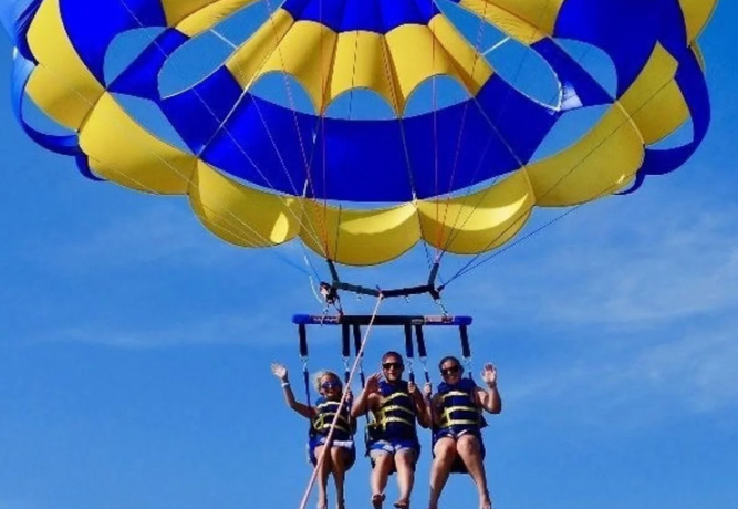 Three people parasailing over palm beach.